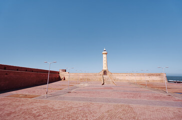 A striking lighthouse surrounded by ancient fort walls under a clear blue sky, located by the...