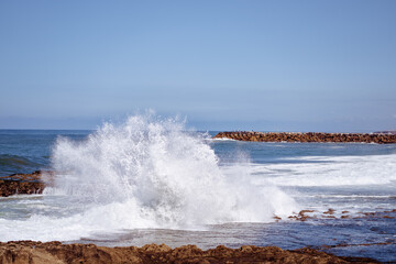 Large ocean waves powerfully crash against rocky coastlines under a clear blue sky, showcasing the beauty and energy of nature by the sea.