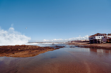 Beautiful coastal scenery featuring crashing waves, a rocky shoreline, and a unique building against a vibrant blue sky, evoking tranquility in a serene, natural beach environment.