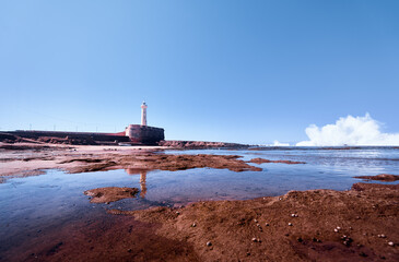 Coastal landscape featuring a lighthouse on a rocky shore, with reflective tide pools and crashing...