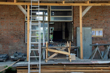 Workers are constructing a building, with scaffolding and materials visible outside a partially finished structure in the countryside