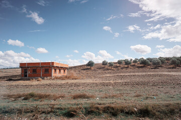 A solitary brick building stands in a barren landscape under a blue sky with scattered clouds....