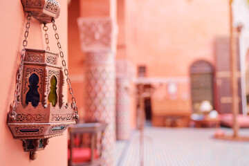 A decorative Moroccan lantern hangs on a wall in a traditional courtyard with intricate tile...