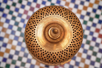 A top view of an ornate brass lamp with intricate cut-out patterns, placed on a colorful mosaic...