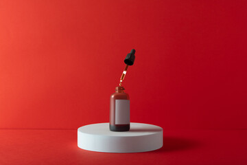 An open amber glass dropper bottle with a blank label for branding, a drop of serum falling from...