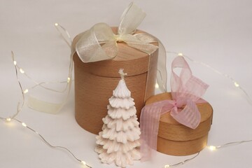 A natural festive composition with wooden gift boxes, a white Christmas tree-shaped candle, and a...