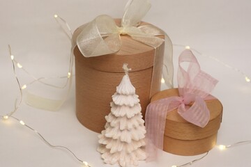 A natural festive composition with wooden gift boxes, a white Christmas tree-shaped candle, and a...