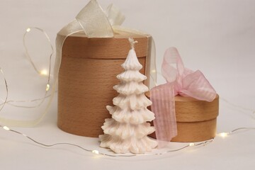 A natural festive composition with wooden gift boxes, a white Christmas tree-shaped candle, and a...