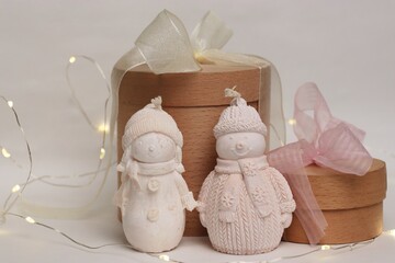 A winter composition with decorative pale pink snowmen, wooden gift boxes, and garlands—a cozy...