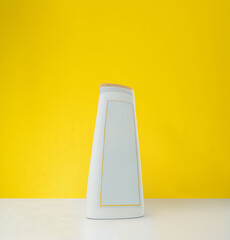 A single white shampoo bottle with a blank label stands on a white surface against a bright yellow...