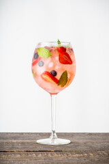 Fresh summer cocktail with strawberry and blueberry in wineglass. Strawberry soda drink on the rustic background.