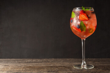 Fresh summer cocktail with strawberry and blueberry in wineglass. Strawberry soda drink on the rustic background.