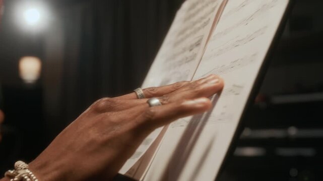 Close up shot of male hand wearing jewelry turning pages of sheet music notes on stand while writing music in studio, copy space