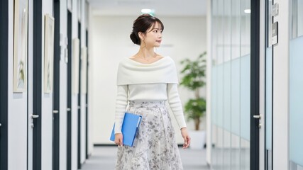 オフィスの廊下で青いファイルを持って颯爽と歩く女性社員