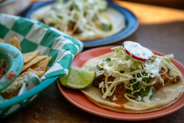 Street-style tacos with lettuce, radish, and lime wedges served alongside tortilla chips in casual setting