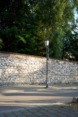 Old street lantern stands near a textured stone wall, bathed in evening light and framed by tall...