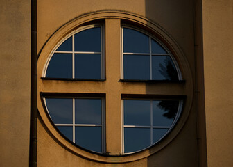 Circular window divided by a cross-shaped frame reflects the evening sky, blending geometry,...