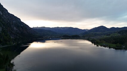 Aerial view of a majestic mountain reflected in a calm lake with clear sky above. Scenic landscape with forested slopes, tranquil water, and peaceful shoreline houses.