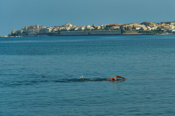 Swimmer in Calm Sea Near Coastal Town