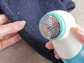 Woman hands holding an electric fabric shaver and lint remover over a dark blue sweater with fabric...