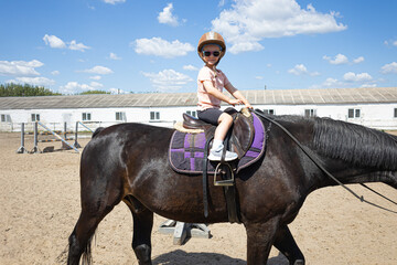 Smiling little girl riding a black horse at equestrian training ground