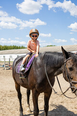 Smiling little girl riding a black horse at equestrian training ground