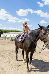 Smiling little girl riding a black horse at equestrian training ground