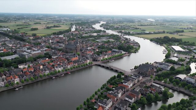 Aerial cityscape view of Deventer, Netherlands, with a river running through it. Old buildings and houses with red rooftops dot the landscape. Shows Dutch culture and travel destinations