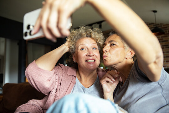 Happy senior lesbian couple taking selfie together on couch at home - Powered by Adobe