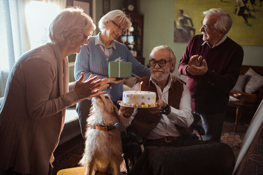 Happy senior man celebrating birthday with friends and dog at home
