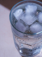 Close-up view of a glass filled with cold water and ice cubes with condensation forming on the...