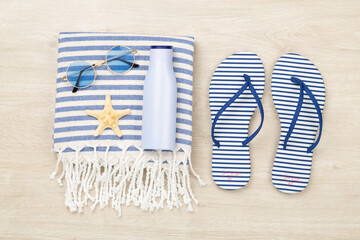 Beach towel with summer accessories on wooden background, top view
