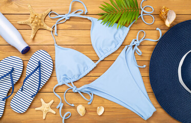Blue bikini with beach accessories on wooden background, top view