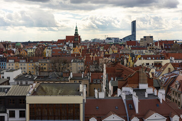 Scenic panoramic view of rooftops in the historic center of Wroclaw, Poland, with colorful facades, church tower and modern skyscraper in background under cloudy sky. Travel, architecture and culture