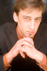 A man in a suit, with his hands clasped under his chin, looking intently at the viewer.