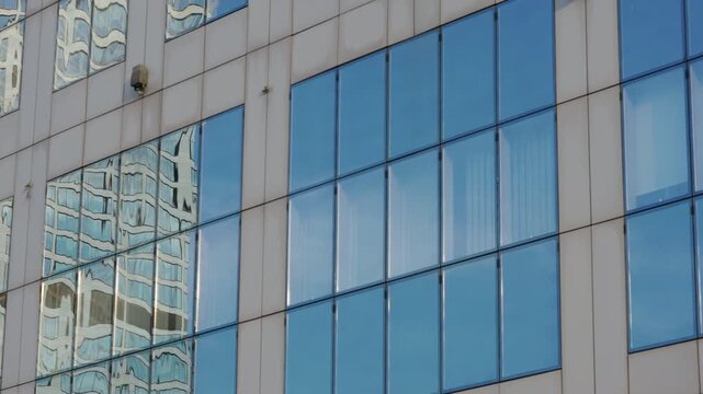 Close-up gimbal or dolly shot of modern skyscraper windows and blue sky mirrored in glass surface, summer day cityscape, high-rise buildings in motion, business district details
