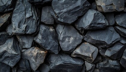 A close-up view of irregularly shaped, dark gray and black volcanic rocks forms a textured wall, with some stones showing hints of brown and lighter gray.