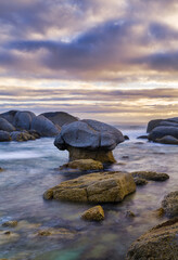Long exposure of Camps Bay sunset with dramatic sky and boulders, Cape Town, South Africa