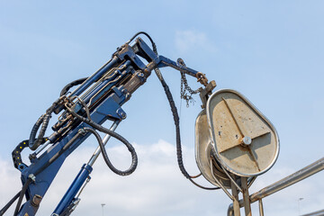 Hydraulic crane lifting a heavy metal pulley with chains and cables on a sunny day