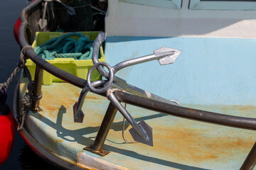Grapnel anchor resting on fishing boat railing in harbor