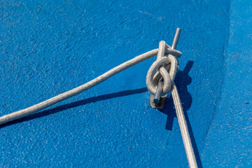 White rope tied around a cleat on blue boat deck