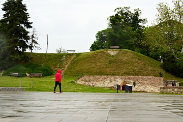 Lonely figure walking in a green park with an ancient wall