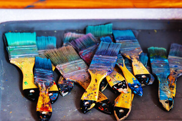 Closeup of many colorful paintbrushes with dried acrylic paint on bristles with artistic splatters,...