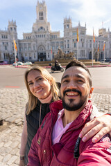 Couple's City Selfie: A smiling couple captures a happy moment during city travel, posing with a historic building, the essence of shared adventure.