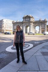 Urban Explorer by the Arch: A traveler finds joy in her journey, she poses in front of a historical landmark with an architectural marvel standing tall against the backdrop of a bustling city.