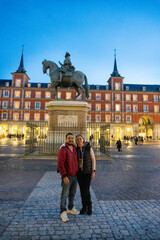 Romantic Evening at Plaza Mayor: A couple stands hand in hand in Plaza Mayor, Madrid, basking in the soft glow of twilight, framed by the iconic architecture and equestrian statue.