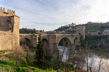 Toledo Bridge: Spain's historic San Martín Bridge, gracefully spanning the Tagus River, is steeped in history and culture, with medieval stone arches, towers, and a timeless design under a sunny sky