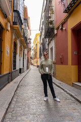 Seville Street Serenity: A vibrant narrow street of Seville invites exploration, adorned with colorful buildings and timeless architecture. A lone figure stands.