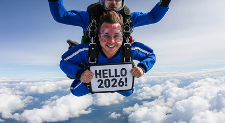 Tandem skydivers in blue suits holding a sign that says HELLO 2026 against a clear sky above the clouds
