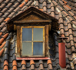 Close up image of an old dormer sticking out of an old tile roof in Europe.